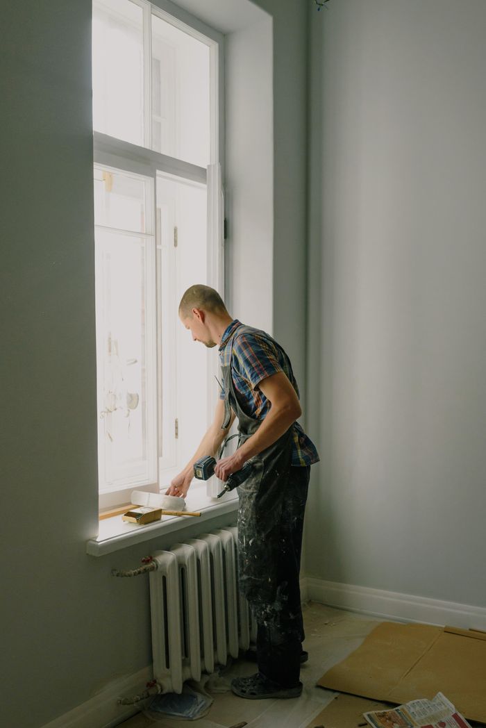 Side view full body of male worker with tool standing near window during renovation works in flat